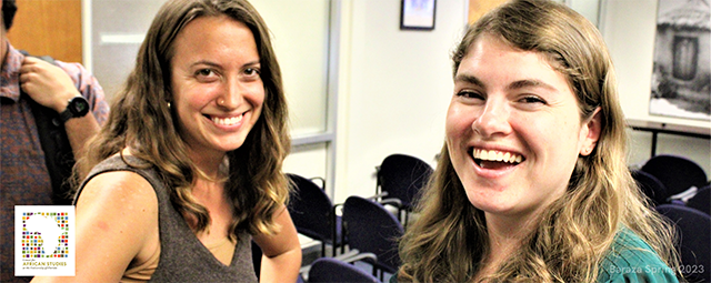 Two women are smiling and looking directly at the camera. They are in a conference room with rows of empty chairs in the background.