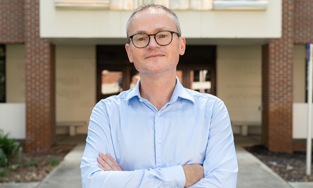 A man smiling, wearing glasses and a dress shirt.