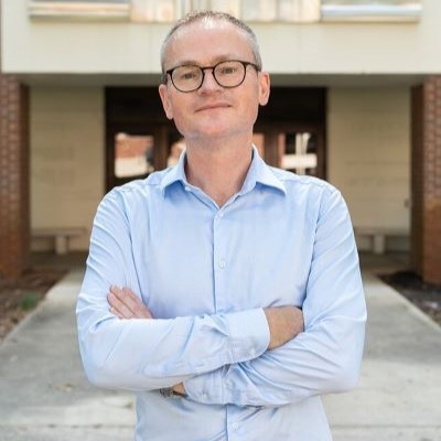 A man smiling, wearing glasses and a dress shirt.