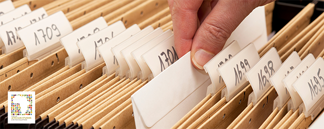 Close-up shot of a hand pulling a document out of a folder that is among many others folders in a filing cabinet drawer.